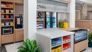 Uma cozinha compacta e moderna, com máquina de café integrada, micro-ondas e prateleiras para armazenamento.