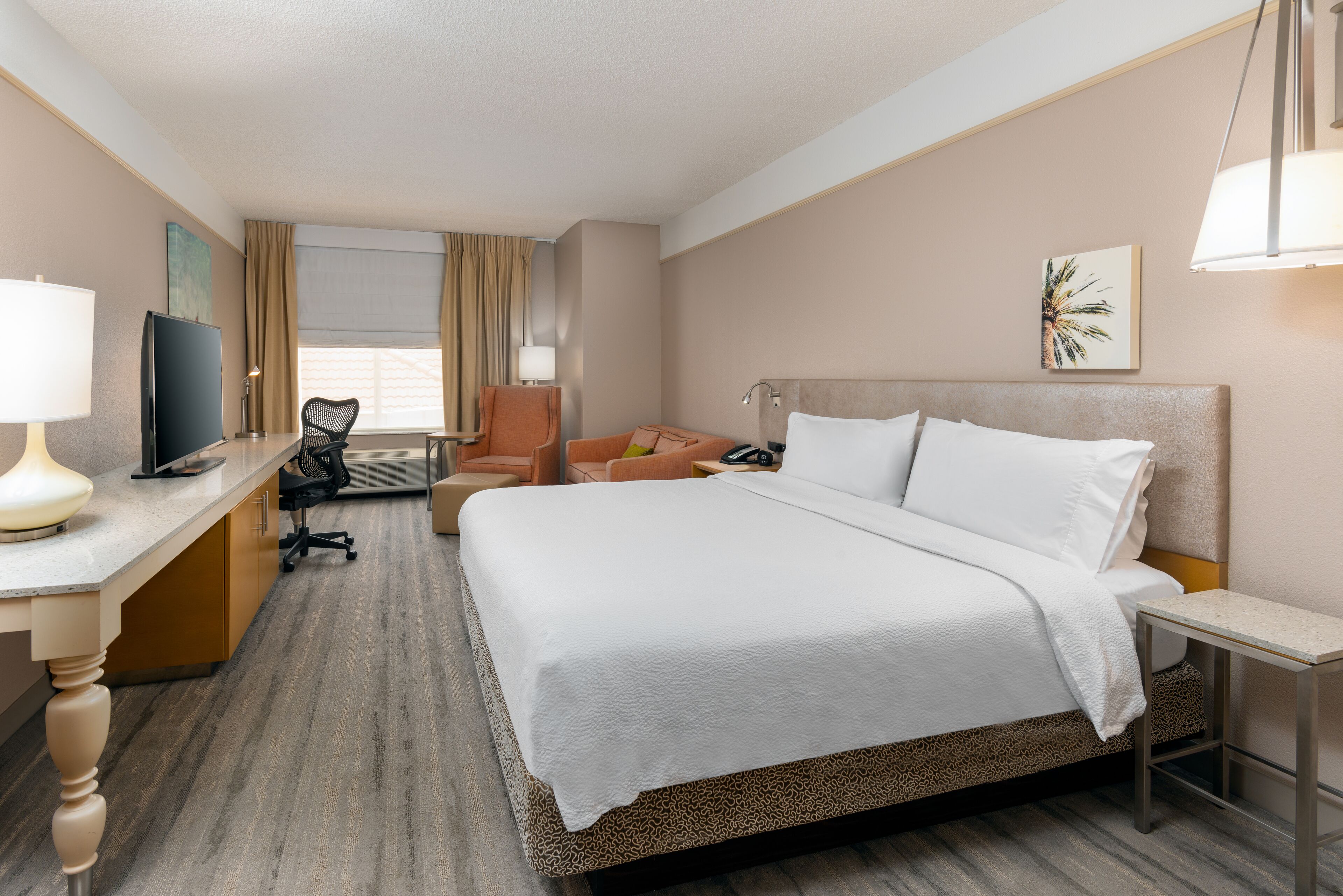 A hotel room with a bed, a desk with a computer, a chair, and a TV.