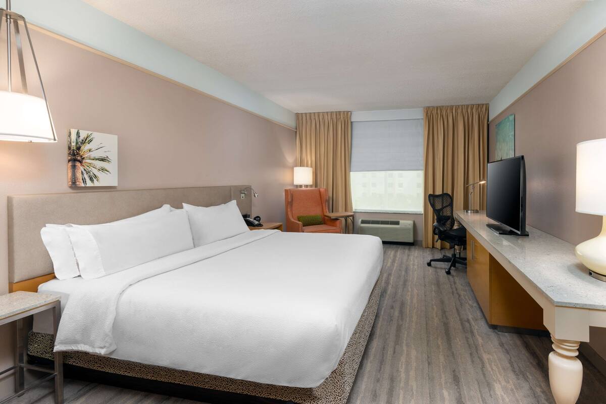 Una camera d'albergo con un letto grande, una scrivania con televisione, una sedia e una finestra con tende.