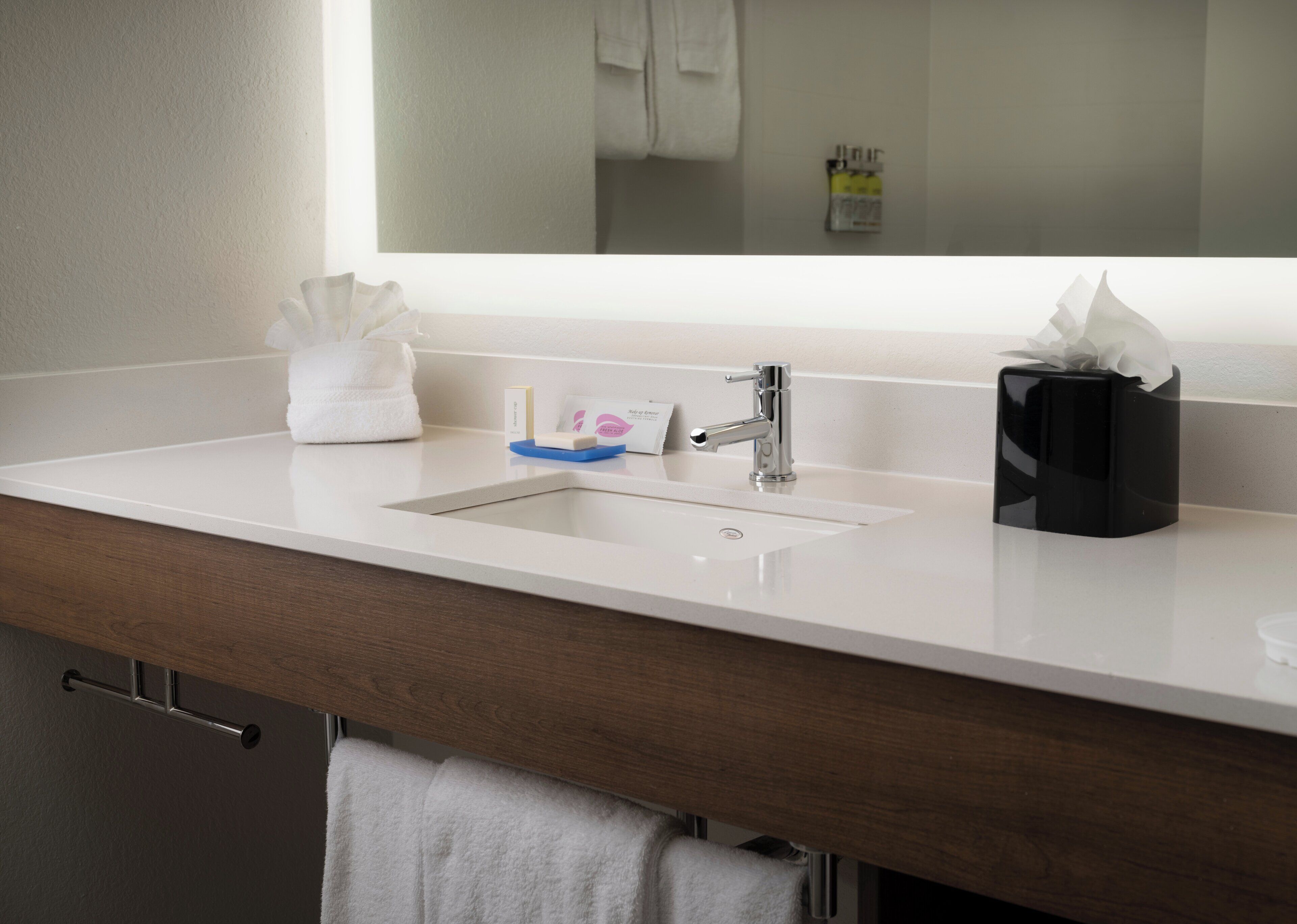 A bathroom with a white sink, a mirror, a towel, a soap dispenser, and a tissue box.