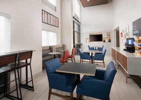 Una cafetería moderna con disposición de mesas, una barra de café y un televisor de pantalla plana.
