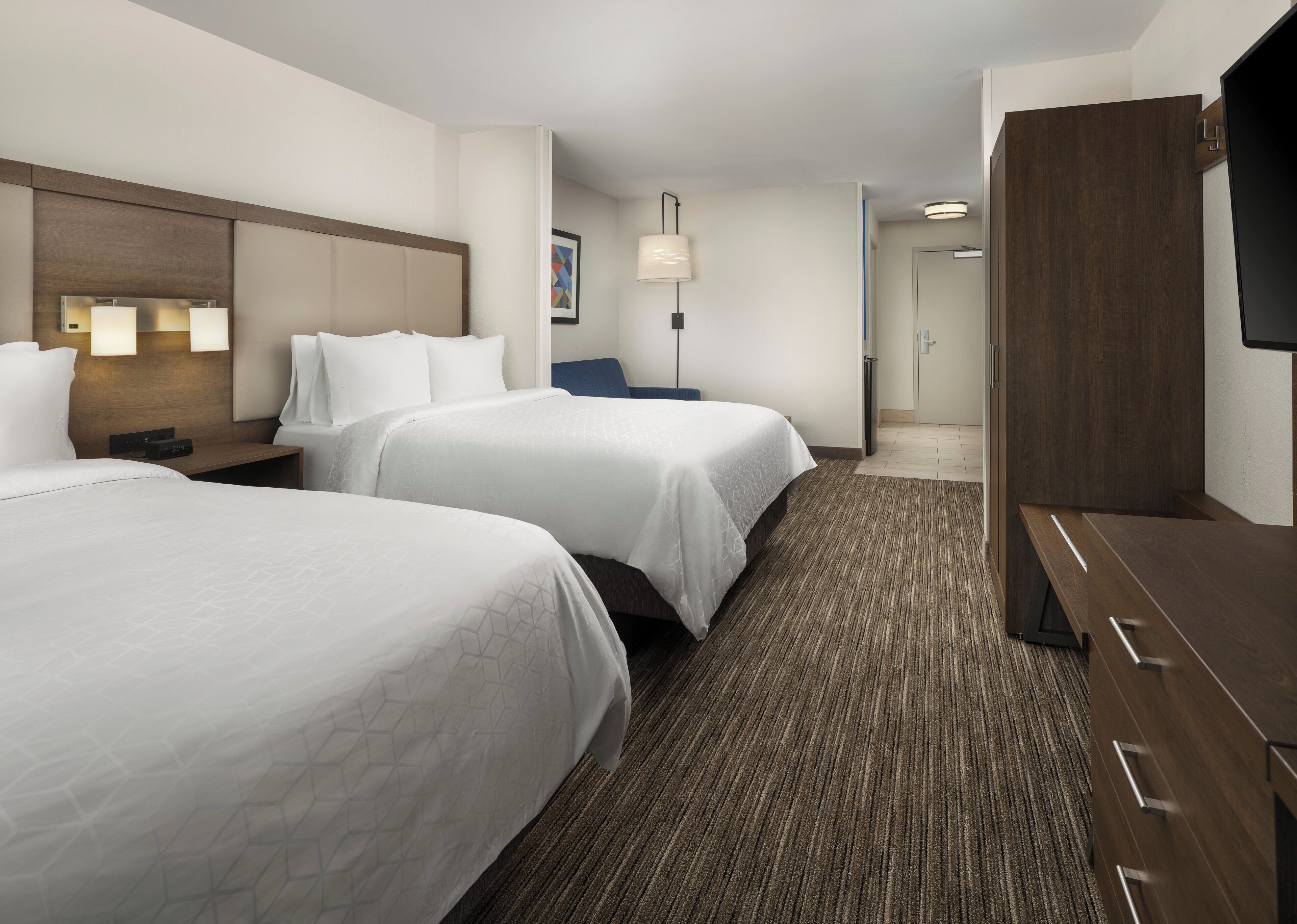 A hotel room with two beds, a desk, a TV, and a door leading to a bathroom.