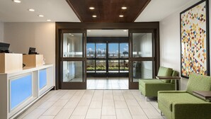 A modern hotel lobby with a reception desk, seating area, and large glass doors leading to a balcony with a city view. - Holiday Inn Express & Suites Olive Branch by IHG (Olive Branch)