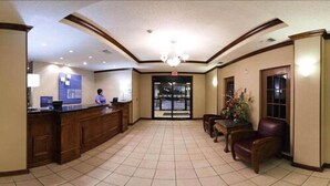 A hotel lobby with a reception desk, a chandelier, a seating area with a table and chairs, and a large door leading outside. - Holiday Inn Express & Suites Plainview by IHG (Plainview)