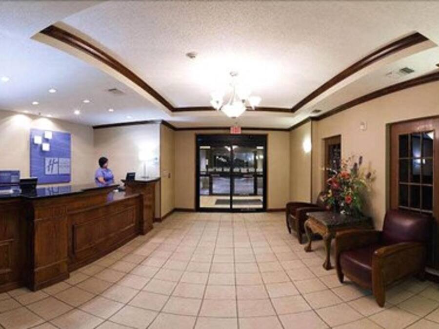 A hotel lobby with a reception desk, a chandelier, a seating area with a table and chairs, and a large door leading outside.