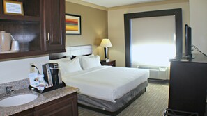 A hotel room with a bed, a desk with a computer, a coffee maker, a lamp, and a large window. - Holiday Inn Express & Suites Plainview by IHG (Plainview)