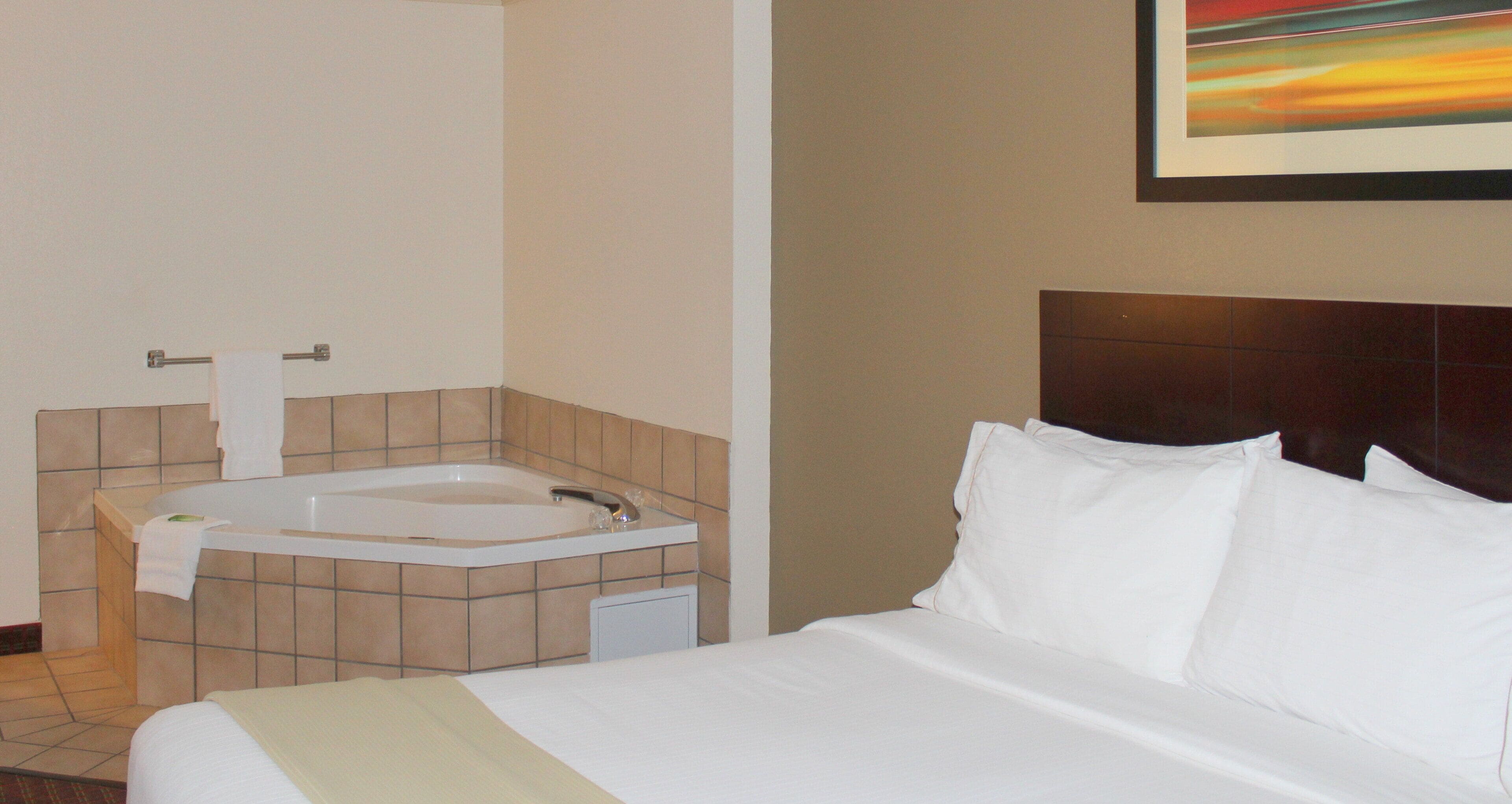 Habitación de hotel con cama, baño con bañera y un cuadro en la pared.