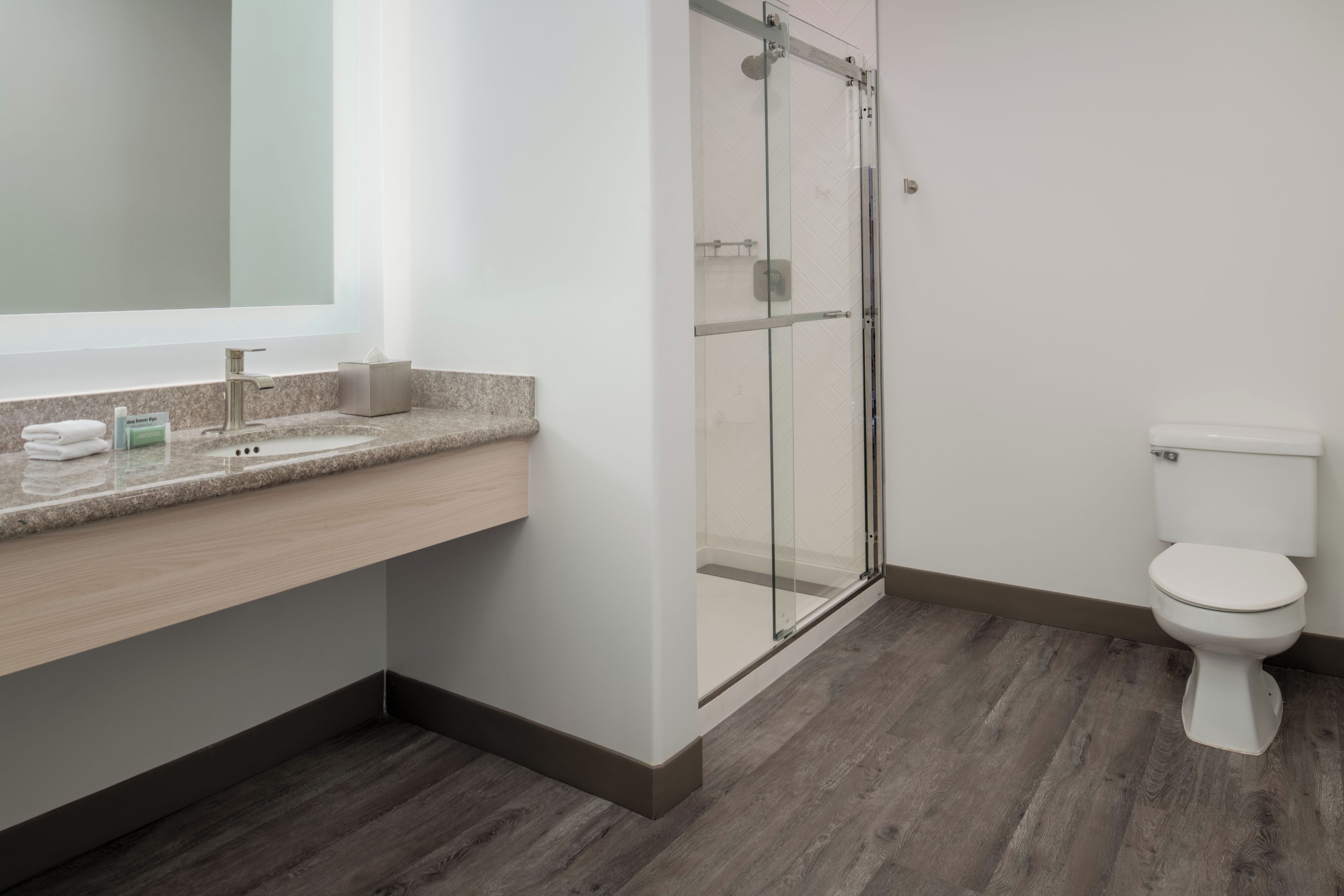 A modern bathroom with a glass shower enclosure, a toilet, and a vanity with a sink and towel rack.