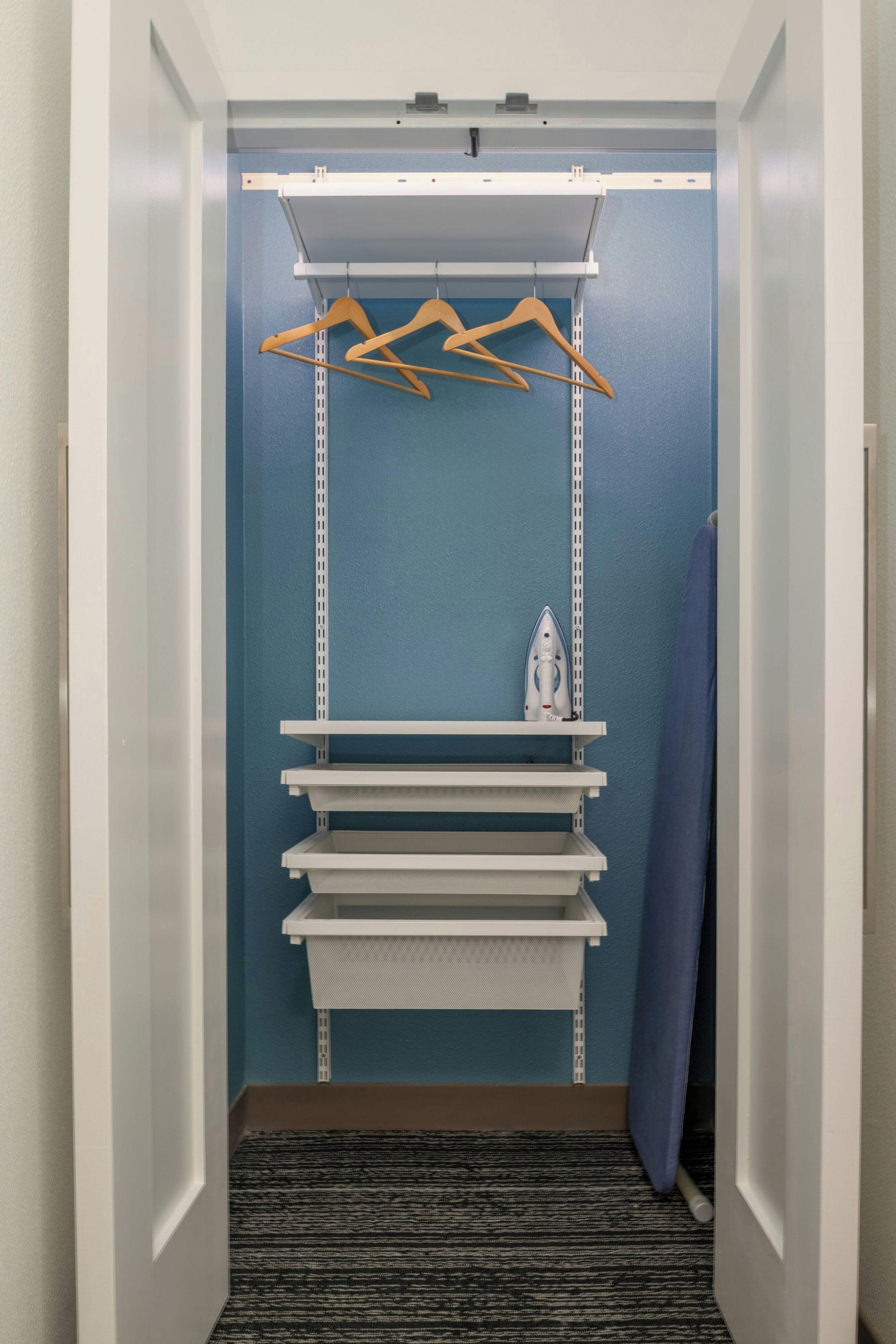 A walk-in closet with a blue wall, white shelving, and a hanging rod.
