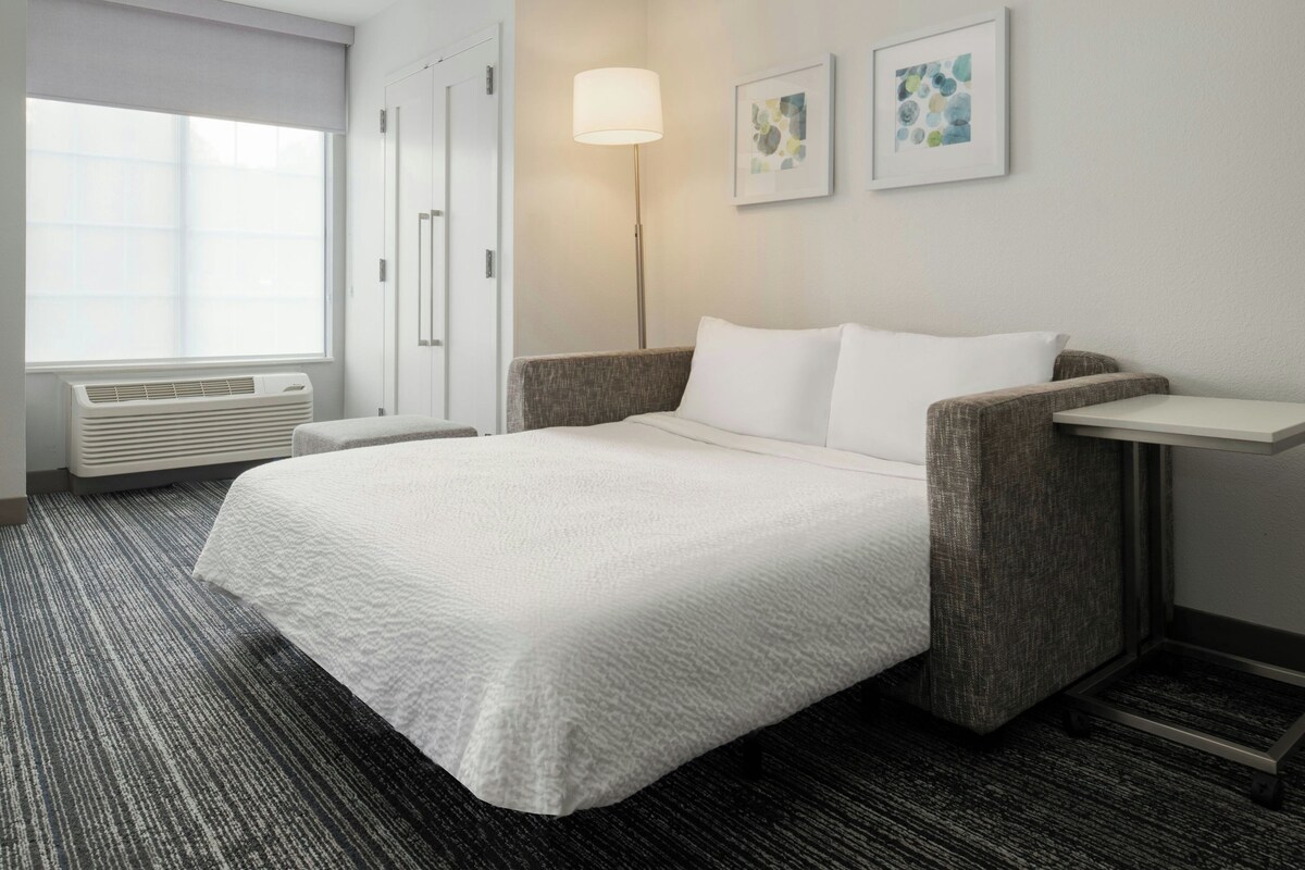 Habitación de hotel con una cama, una mesita de noche, una lámpara y dos obras de arte enmarcadas en la pared.