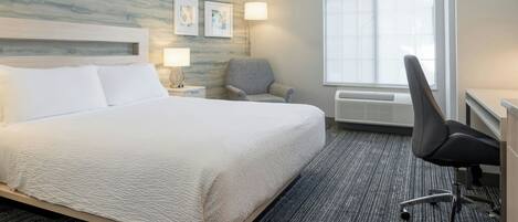 A hotel room with a large bed, a chair, a desk, a lamp, and a window.