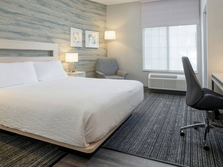 Una habitación de hotel con una cama grande, una silla, un escritorio, una lámpara y una ventana.