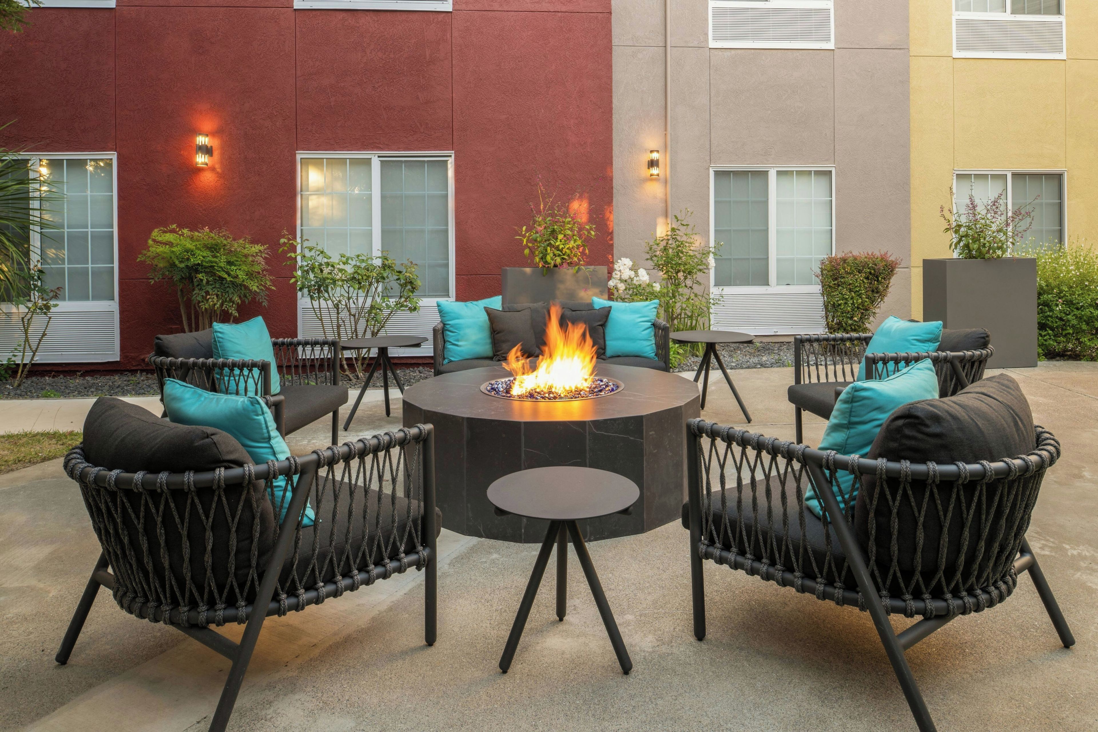 A circular outdoor seating area with a fire feature, surrounded by wicker chairs with cushions.