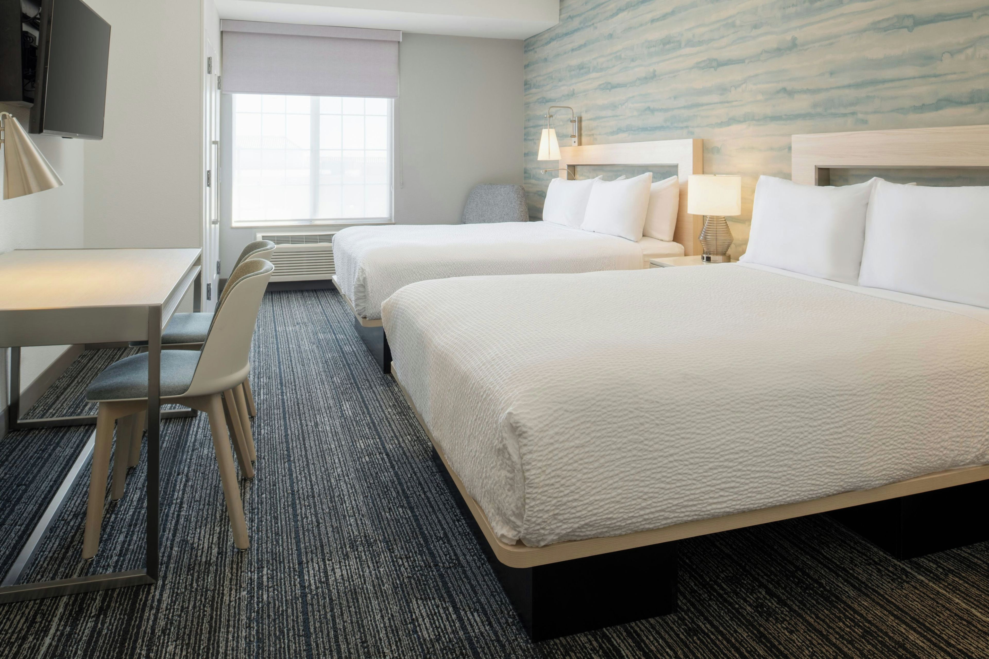 A hotel room with two beds, a desk, a chair, and a TV.