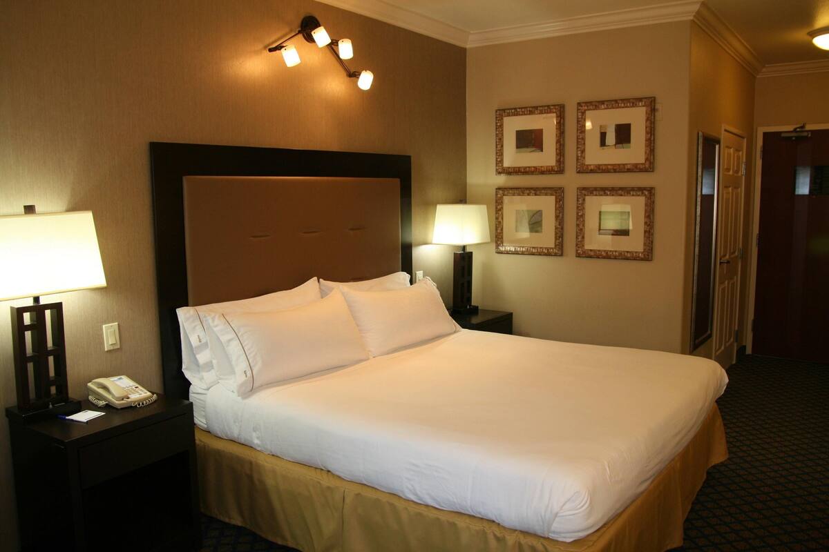 A hotel room with a large bed, two bedside tables, a telephone, and four framed pictures on the wall.