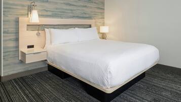 A hotel room with a bed, a nightstand, a wall-mounted lamp, and a carpeted floor.
