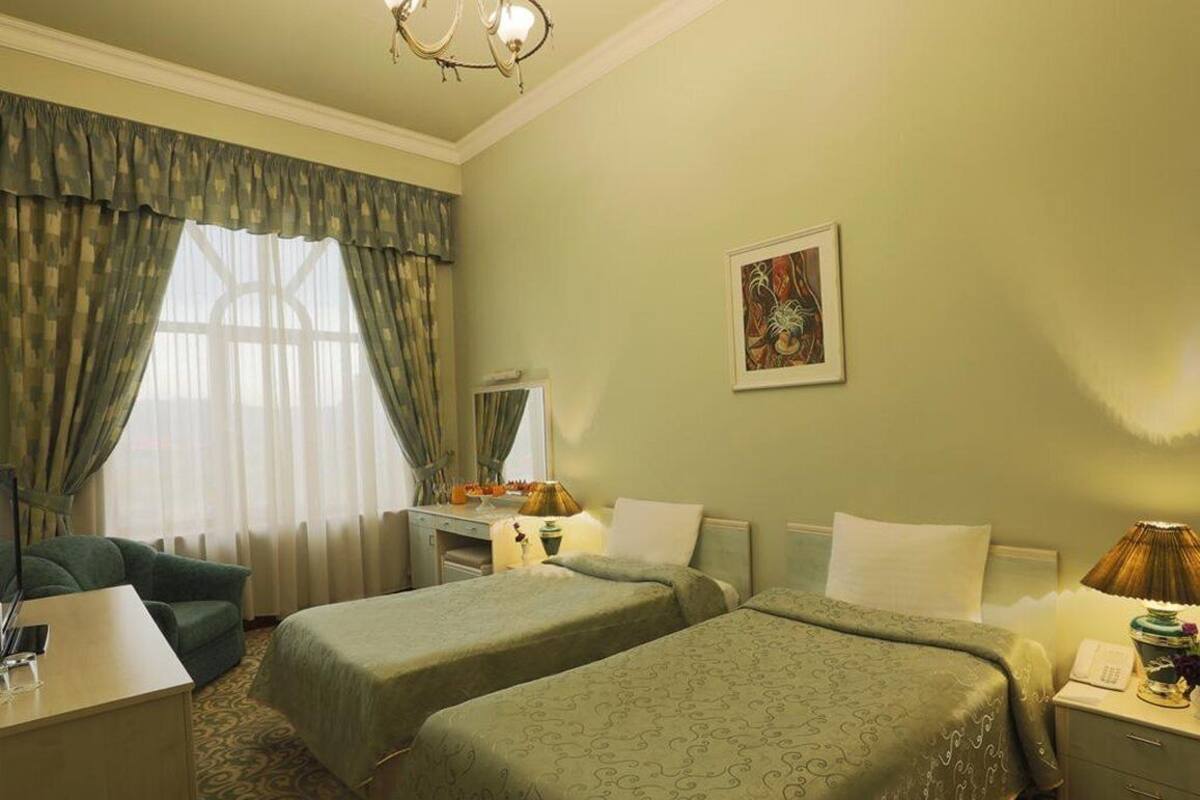 A hotel room with two beds, a desk, a chair, a lamp, and a painting on the wall.