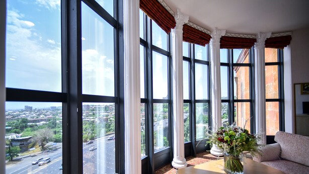 Una habitación con ventanas amplias, un sofá, una mesa y un jarrón con flores.
