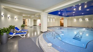 Una piscina interior con sillas reclinables azules y plantas en macetas.