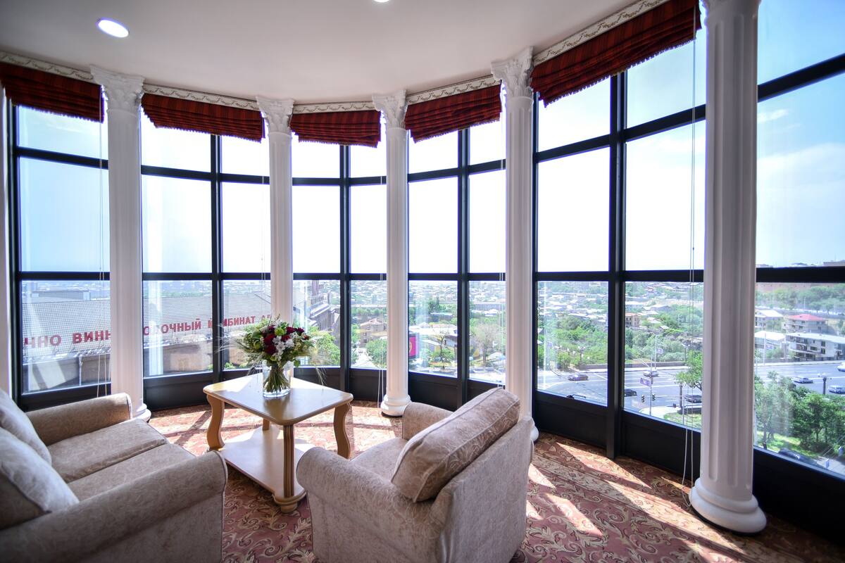 A corner room with large windows, a table with a vase, and two armchairs.