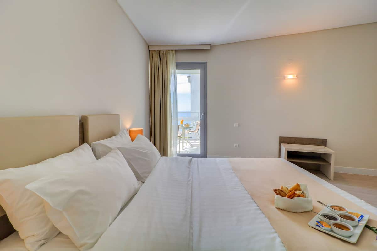 Ein Hotelzimmer mit Bett, einem kleinen Tisch mit Brot und Beilagen, Blick auf den Balkon und einer Tür, die nach draußen führt.