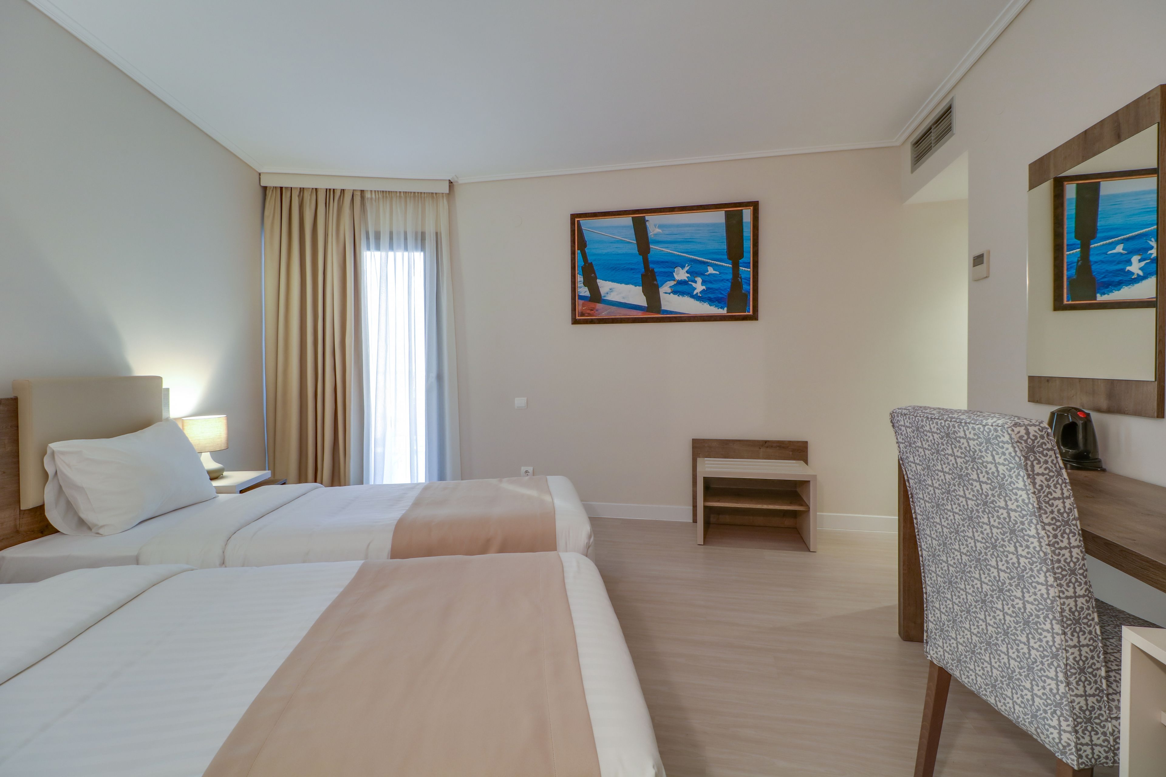 A hotel room with two beds, a desk, a chair, and artwork on the walls.