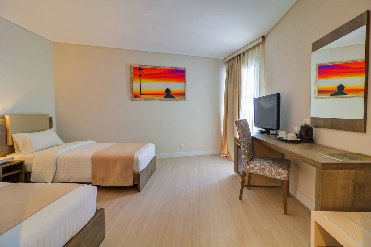 Ein Hotelzimmer mit zwei Betten, einem Schreibtisch mit Stuhl, einem Fernseher und zwei Bildern an der Wand.
