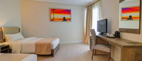 Habitación de hotel con dos camas, un escritorio con una silla, un televisor y dos cuadros en la pared.