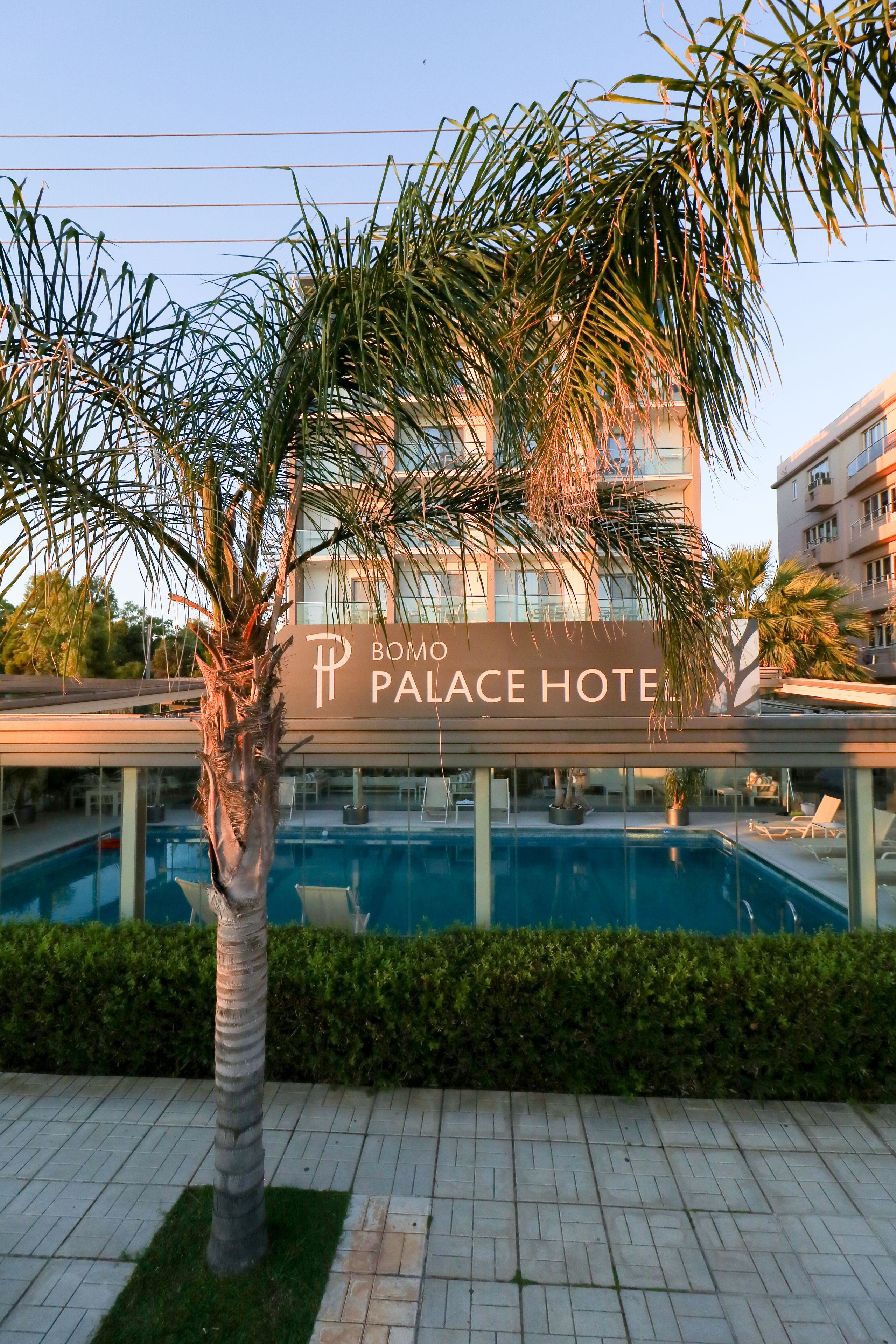 Un hotel moderno con zona de piscina, palmeras y un cartel que dice "BOMO PALACE HOTEL".