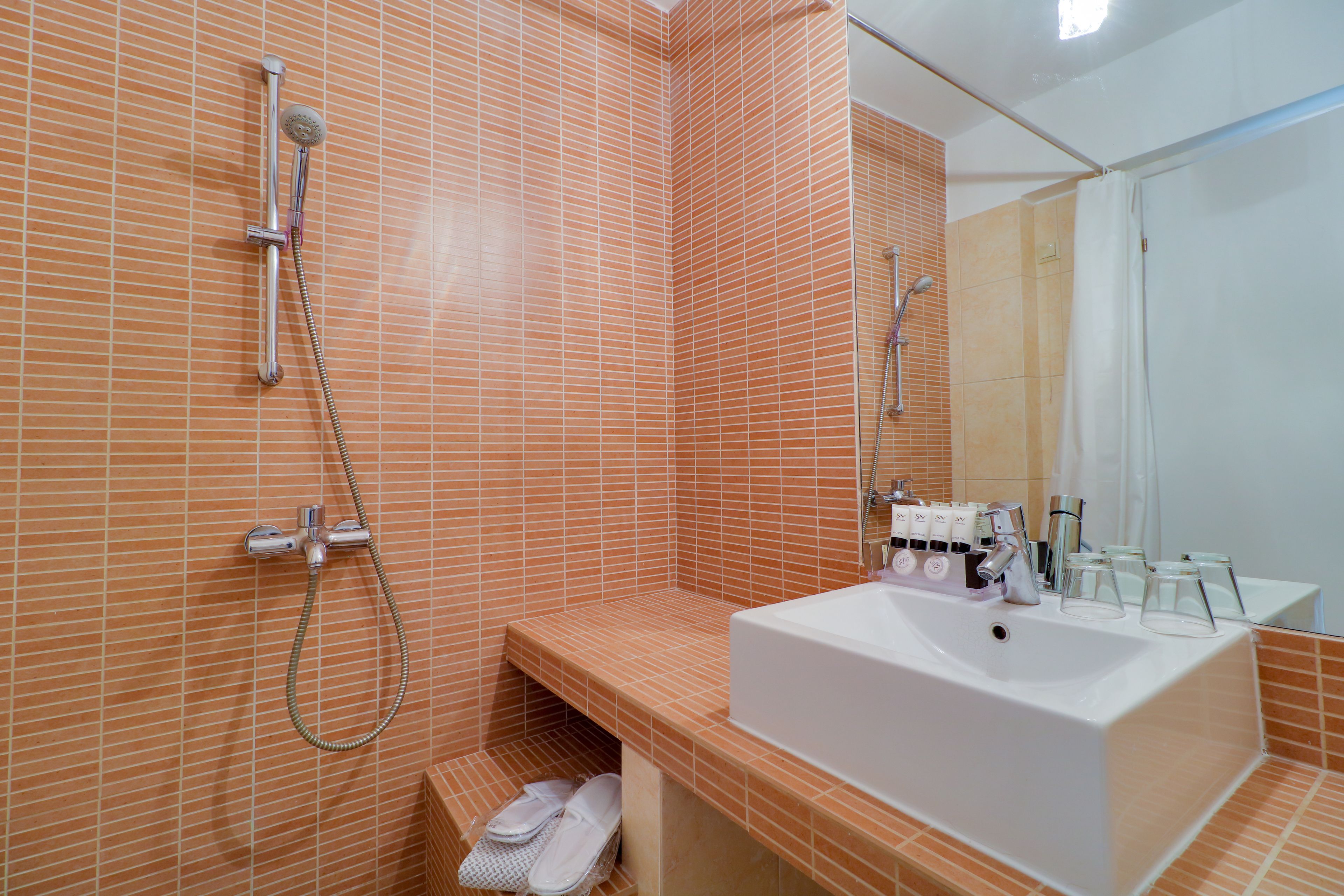 Une salle de bain avec des murs recouverts de carreaux orange, un lavabo blanc et un espace douche.