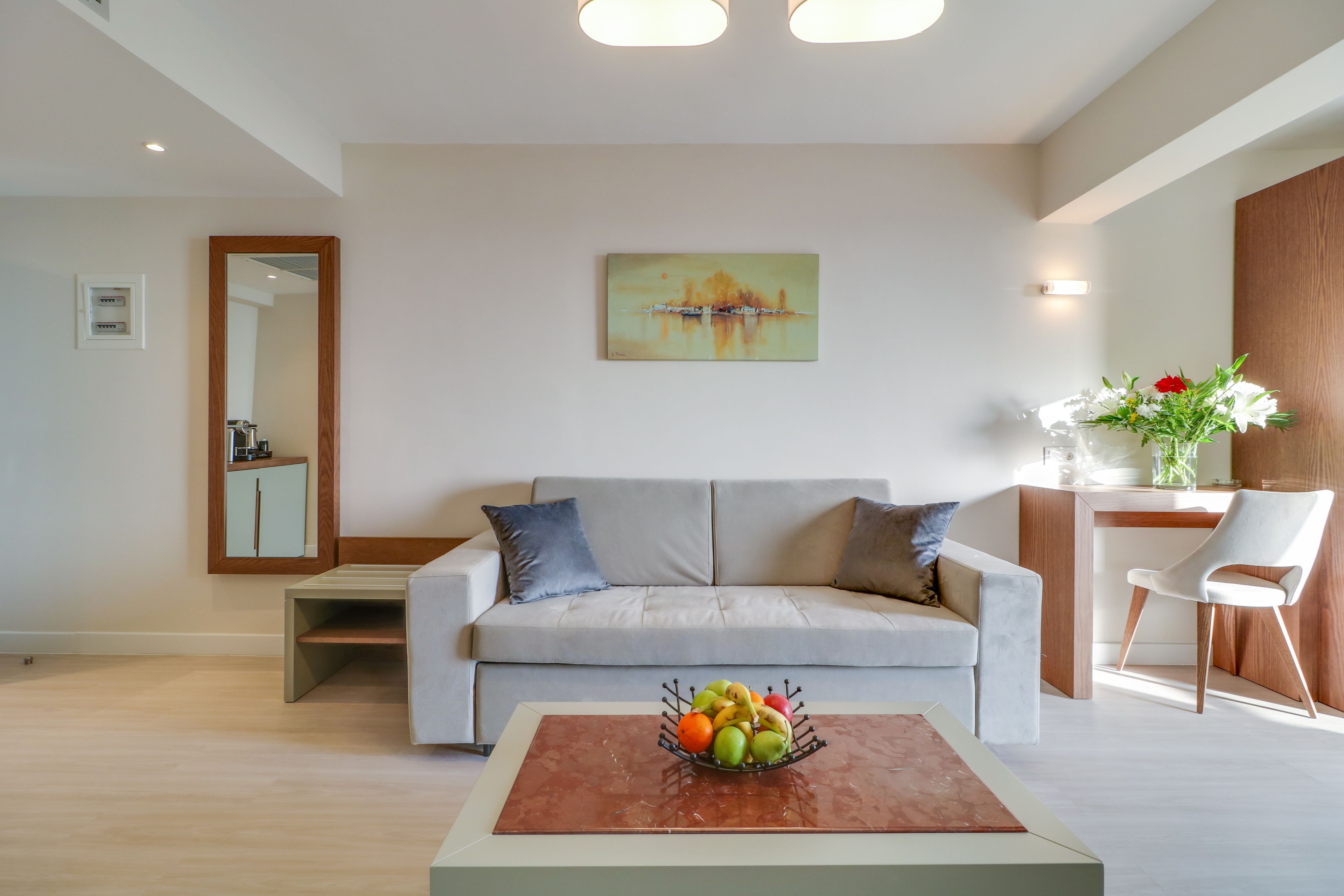 Una sala de estar moderna con un sofá gris, una mesa de centro con fruta, un cuadro en la pared y un mueble de madera.