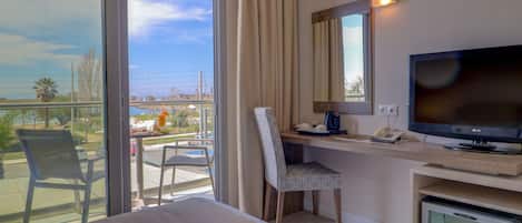 A hotel room with a bed, a desk with a computer, a chair, a television, and a minibar.