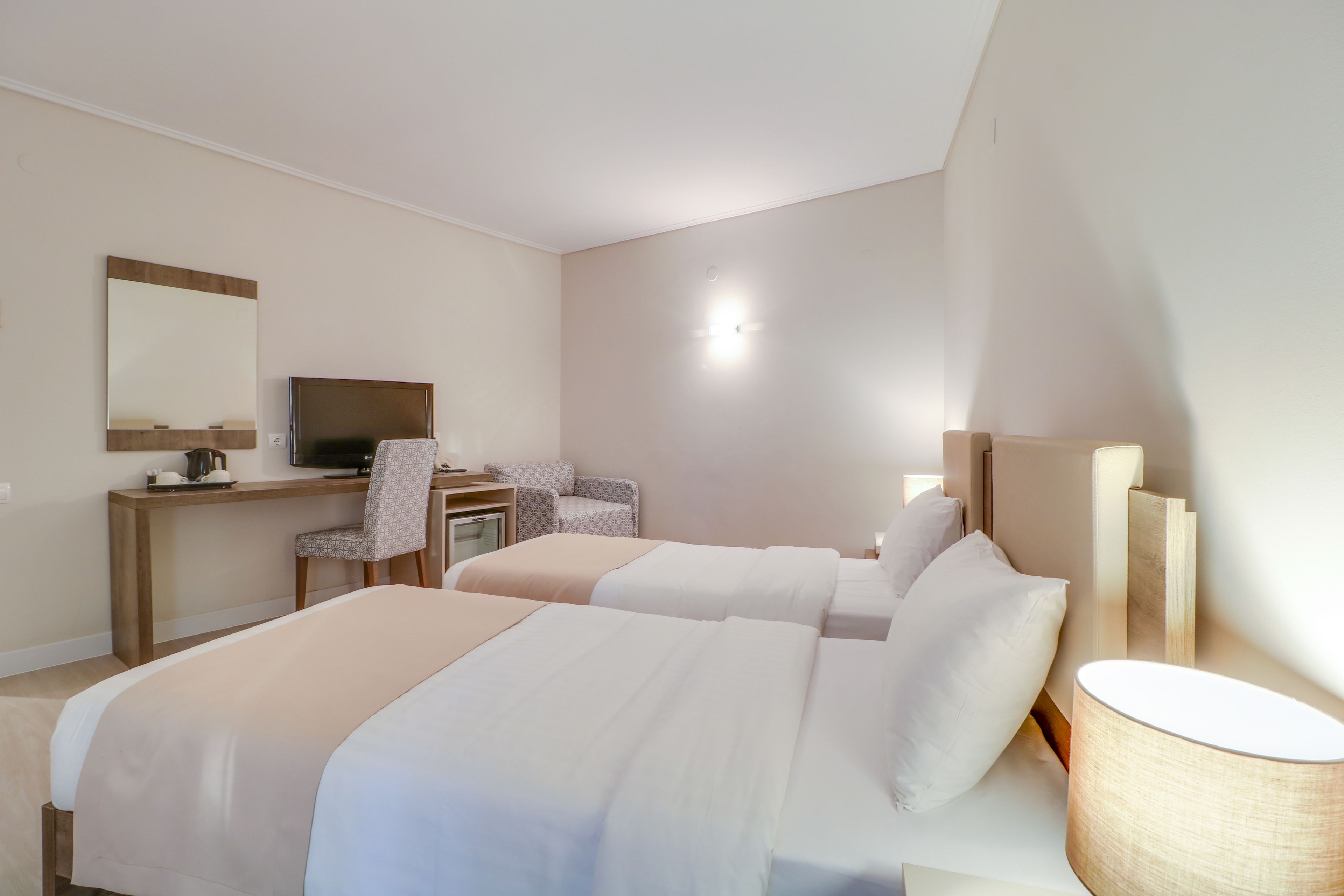 Habitación de hotel con dos camas, un escritorio, una silla, un televisor y una lámpara.