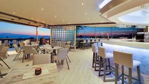 Een modern restaurant met een bar, zitplaatsen en een uitzicht op de stadshemel in de schemering.