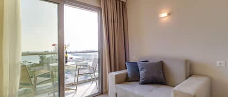 Un salon moderne doté d’une grande porte-fenêtre coulissante donnant sur un balcon, d’un canapé beige agrémenté de coussins et d’une petite table avec des chaises.