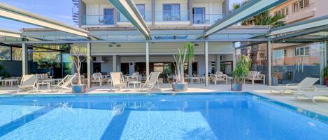 Un hôtel moderne doté d’une piscine, de chaises longues et d’un espace extérieur couvert.