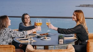 Drie personen proosten aan een ronde tafel met uitzicht op zee.