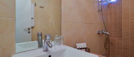 A bathroom with a white sink, a mirror, a shower, and a tiled wall.