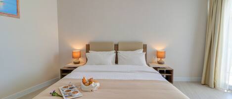 A hotel room with a large bed, two bedside tables with lamps, a tray with breakfast items, and a painting on the wall.