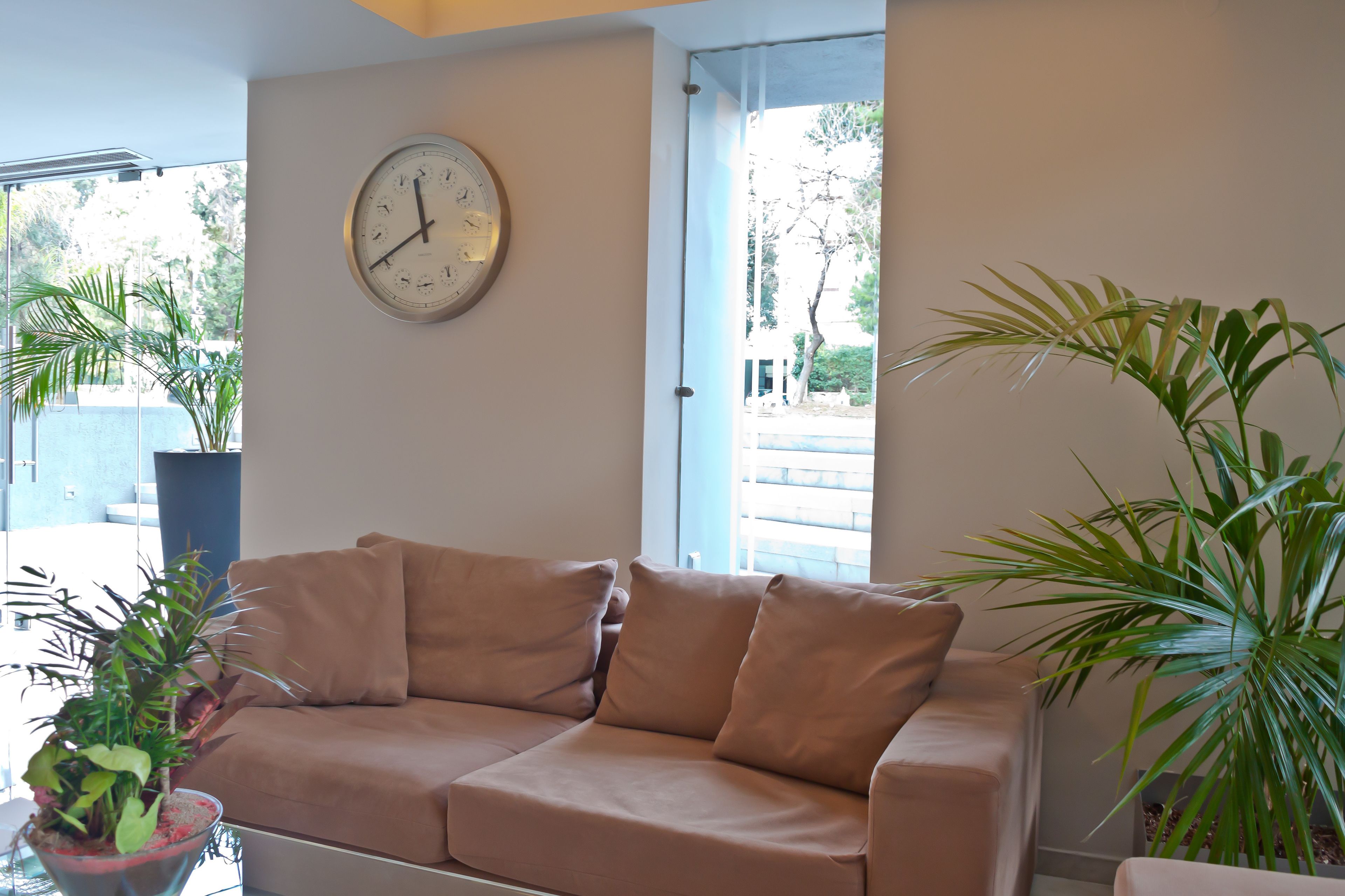 A beige sofa with a wall clock, a potted plant, and a view through a window.