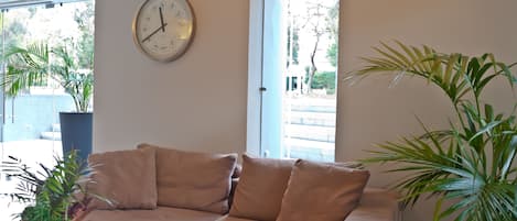 A beige sofa with a wall clock, a potted plant, and a view through a window.