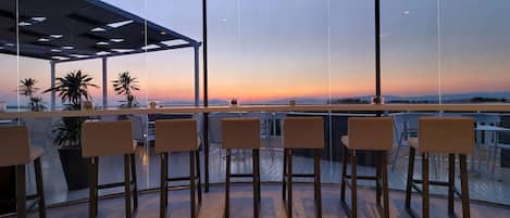 Zona de bar moderna con vista panorámica del atardecer sobre el océano.