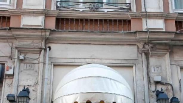 L’entrée d’un hôtel, avec un tapis rouge, un auvent blanc et des panneaux indiquant le nom de l’hôtel.