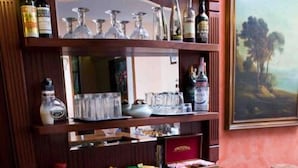 Un coin bar avec des étagères remplies de bouteilles et de verres, un plateau sur lequel reposent deux tasses de café et un tableau accroché au mur.