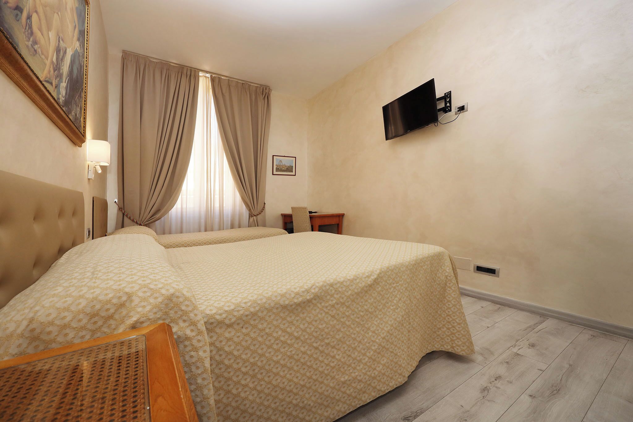 A hotel room with two beds, a television mounted on the wall, a desk, and a window with curtains.