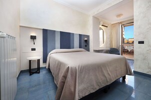 Habitación de hotel con cama, una mesita, una silla, un radiador y vistas al exterior.