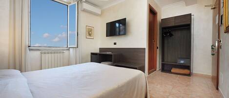 A hotel room with a large bed, a television mounted on the wall, a wardrobe, and a window with curtains.