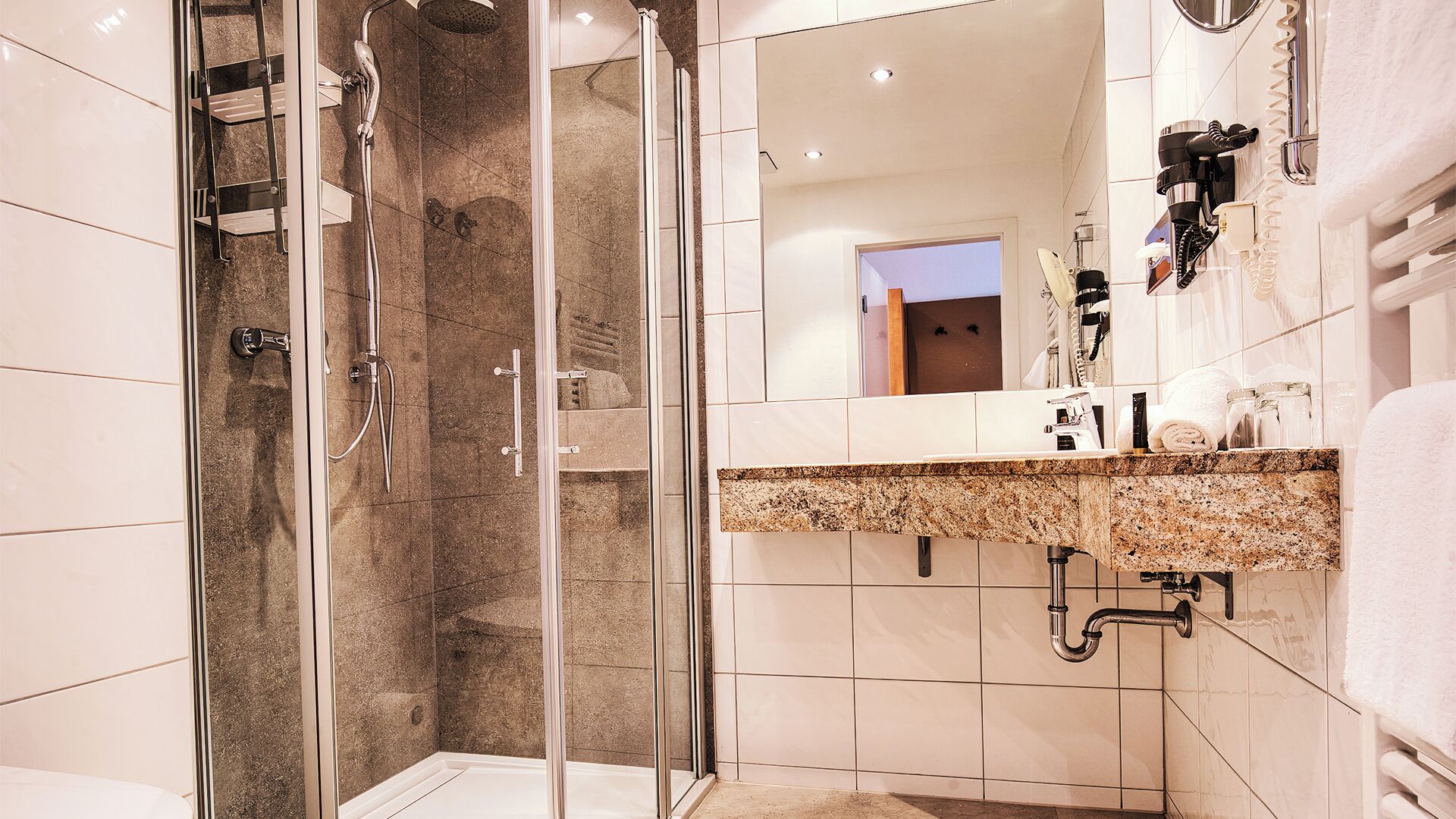 Ein modernes Badezimmer mit einer Duschkabine, einem Waschtisch mit Granitplatte und einem großen Spiegel.