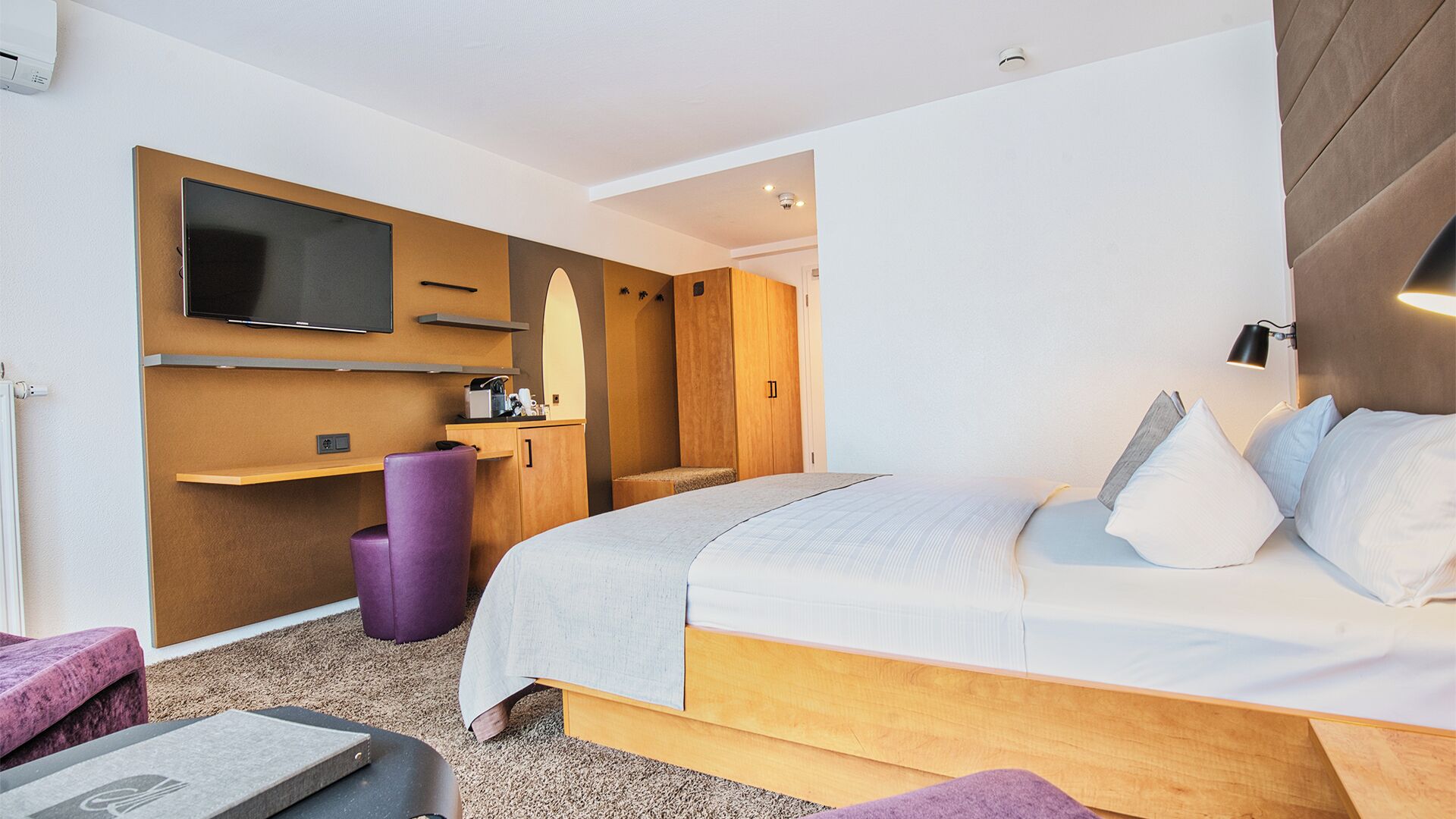 A modern hotel room with a large bed, a desk, a chair, and a television.