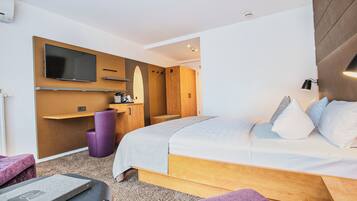 A modern hotel room with a large bed, a desk, a chair, and a television.